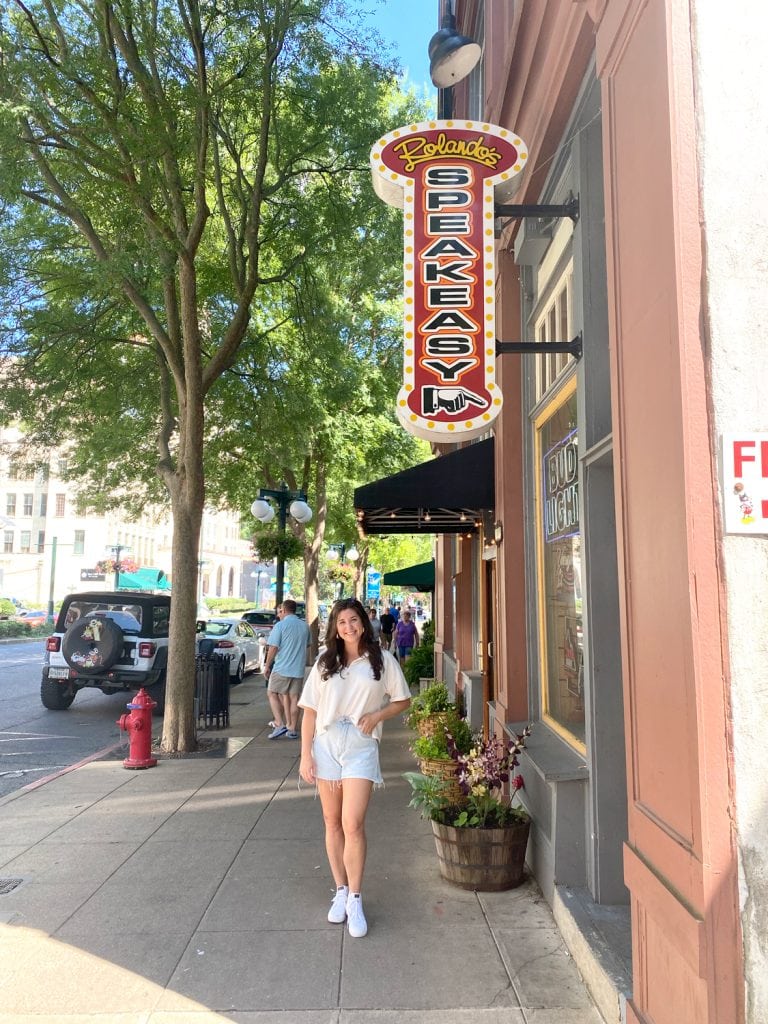A girl standing under the sign that says Rolando's speakeasy.