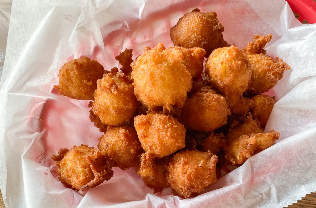 A close up of a container of fried hushpuppies. They are golden and look delicious. 