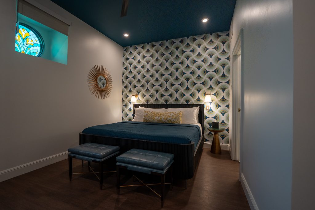 A room at the Star on Spring in Springdale, Arkansas. The bedspread is blue and the high ceiling is painted blue. There is modern wallpaper on the back wall. 