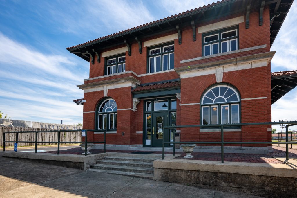 Beautiful old restored train depot in Helena, Arkansas. This is a two story red brick structure with a symmetrical shape. There are two  arched windows flanking the door. The trim is painted green. 