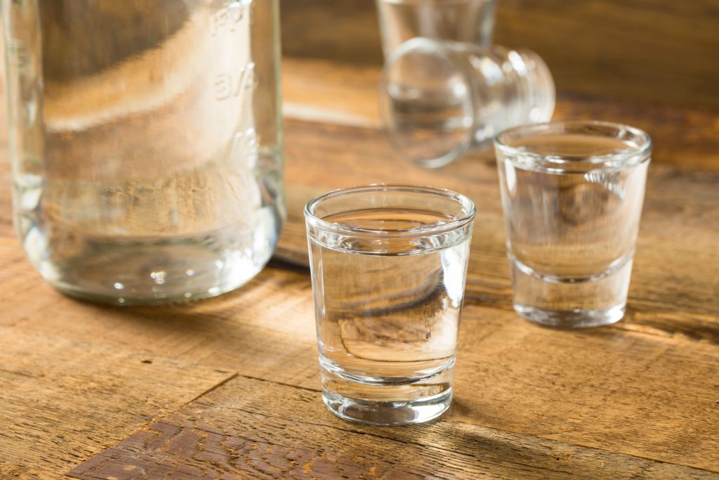 Bottle and two shot glasses of what looks like moonshine. The Ozark Moonshine and Music Festival is one of the Festivals in Arkansas in November. 