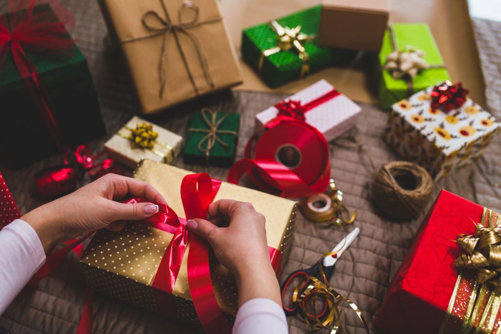 You see a woman's hands tying a red ribbon on a wrapped Christmas gift. Holiday markets are one of the best Christmas events in Fayetteville, arkansas.