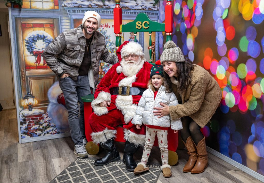 A family standing with their young daughter with Santa Clause.