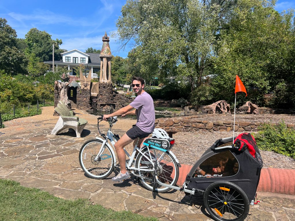 Young man on a bike pulling a baby carrier near Wilson Park in Fayetteville.